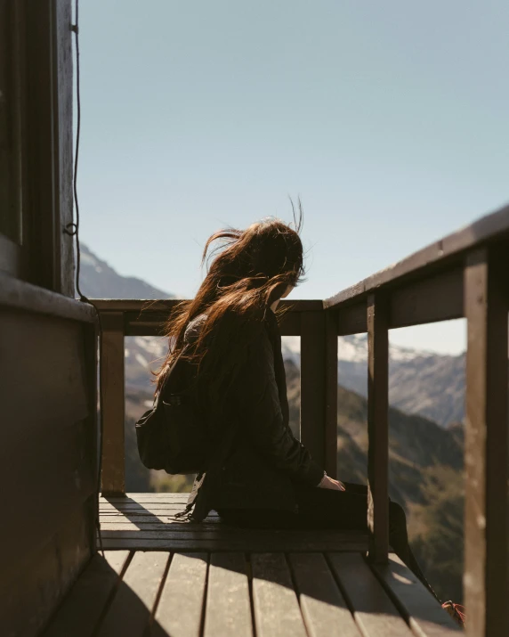 a woman sits on a porch while looking out into the mountains