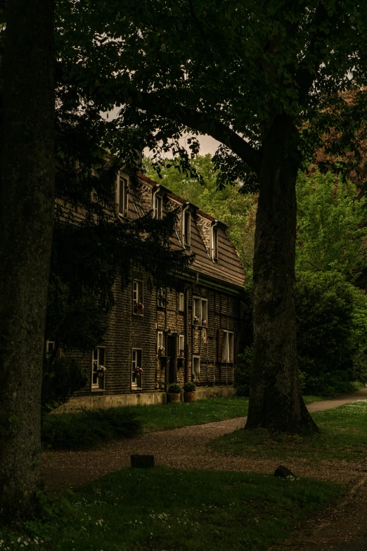 the house is dark and has some green trees in front of it