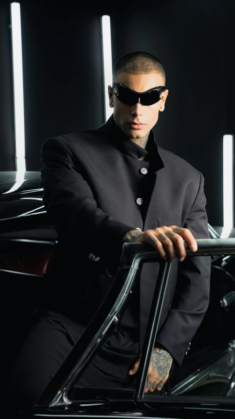 a man with sunglasses on his head standing in front of a black car