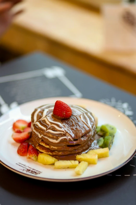 a chocolate pancake with fruit sits on a white plate