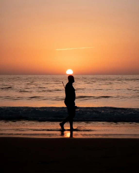 a silhouetted man walking on a beach with the sun setting in the background