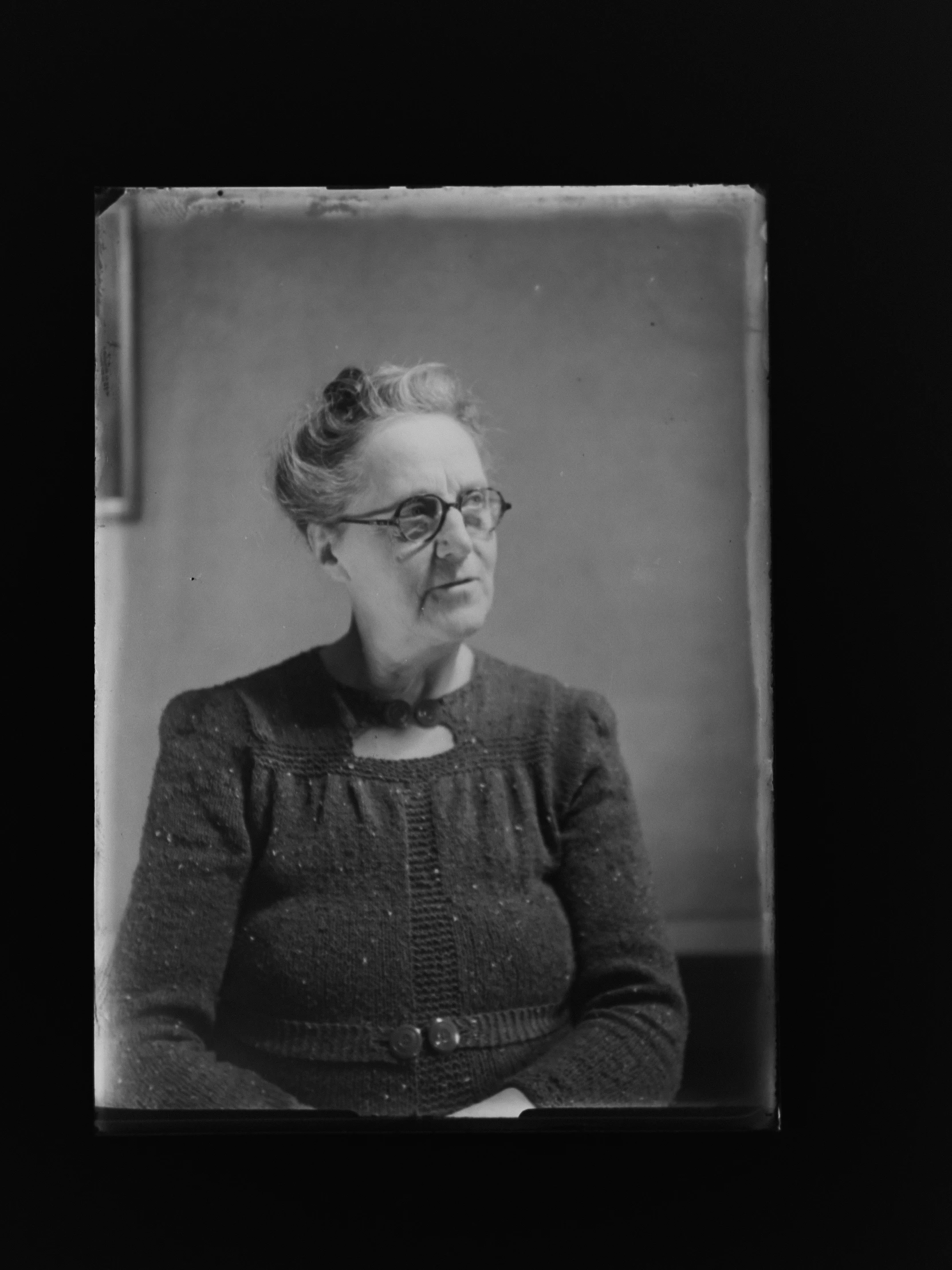 an old woman wearing glasses sitting next to a white wall