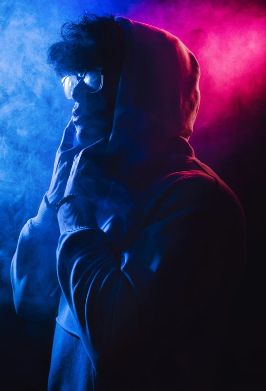 a man in glasses holding his head in front of blue and red smoke
