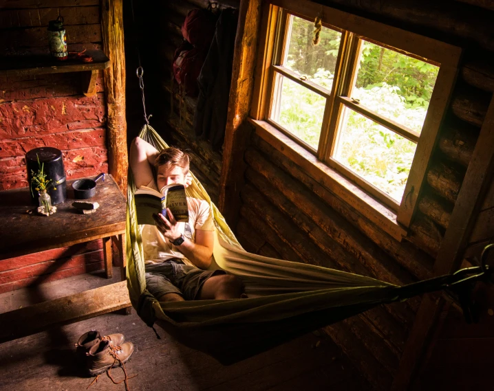 the two men sit inside of a hammock looking out the window