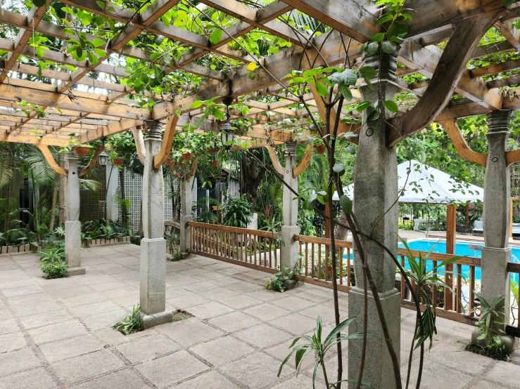 the view of a very nice outdoor swimming pool from inside an open pergola