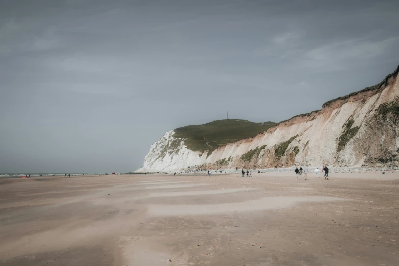 people standing on a beach near a white cliff