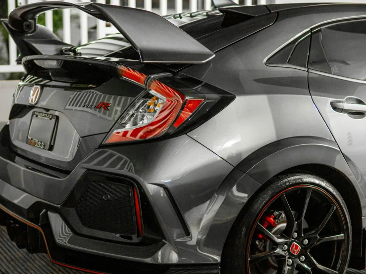 a grey honda civic type type car in front of a white fence