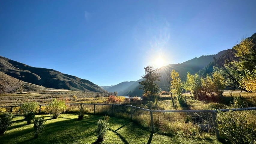 a view of a field with mountains, trees and a fence