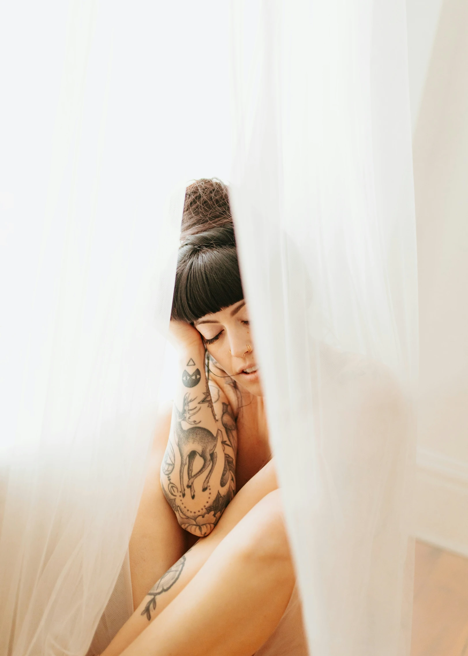 a tattooed woman is sitting on her bed with her head turned away from the camera