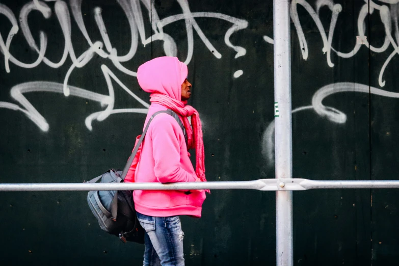 a young woman in a pink jacket and jeans walks