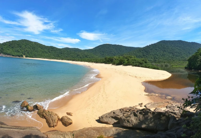 a sandy beach with white sand and water and a few rocks on the shore