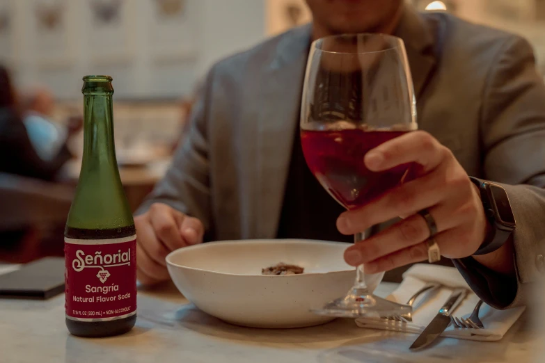 a man sitting at a table with wine, a bowl of food and bottle of alcohol