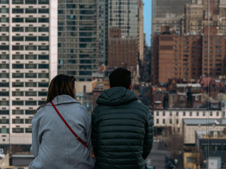 two people sitting on a ledge overlooking buildings and a city