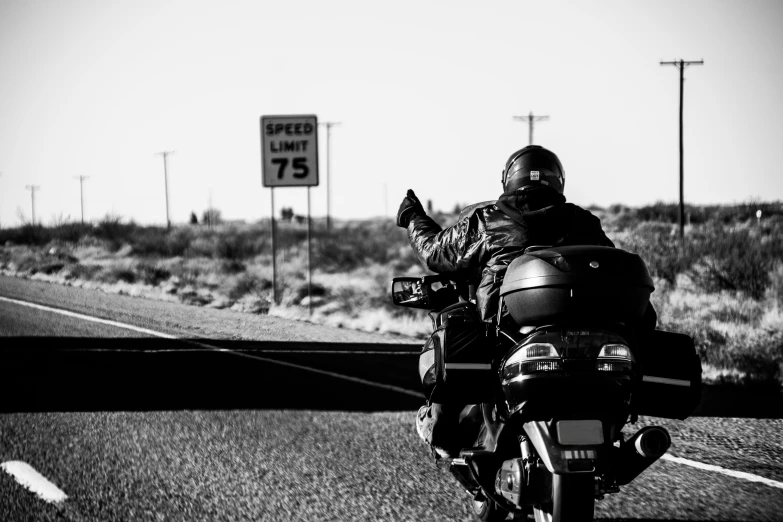 a motorcycle rider driving down the road with a speed limit sign in the background