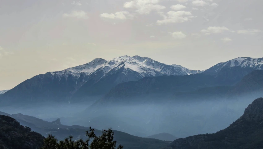 snow covered mountain range in the middle of a cloudgy sky