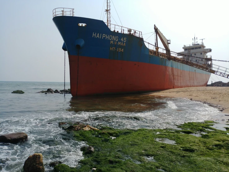 large ship sitting on shore next to rocky area