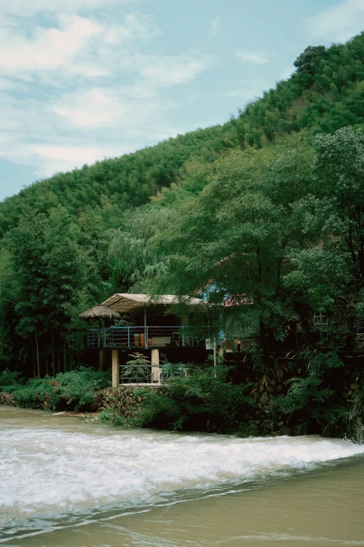 an old house on a beach near a tree - lined mountain