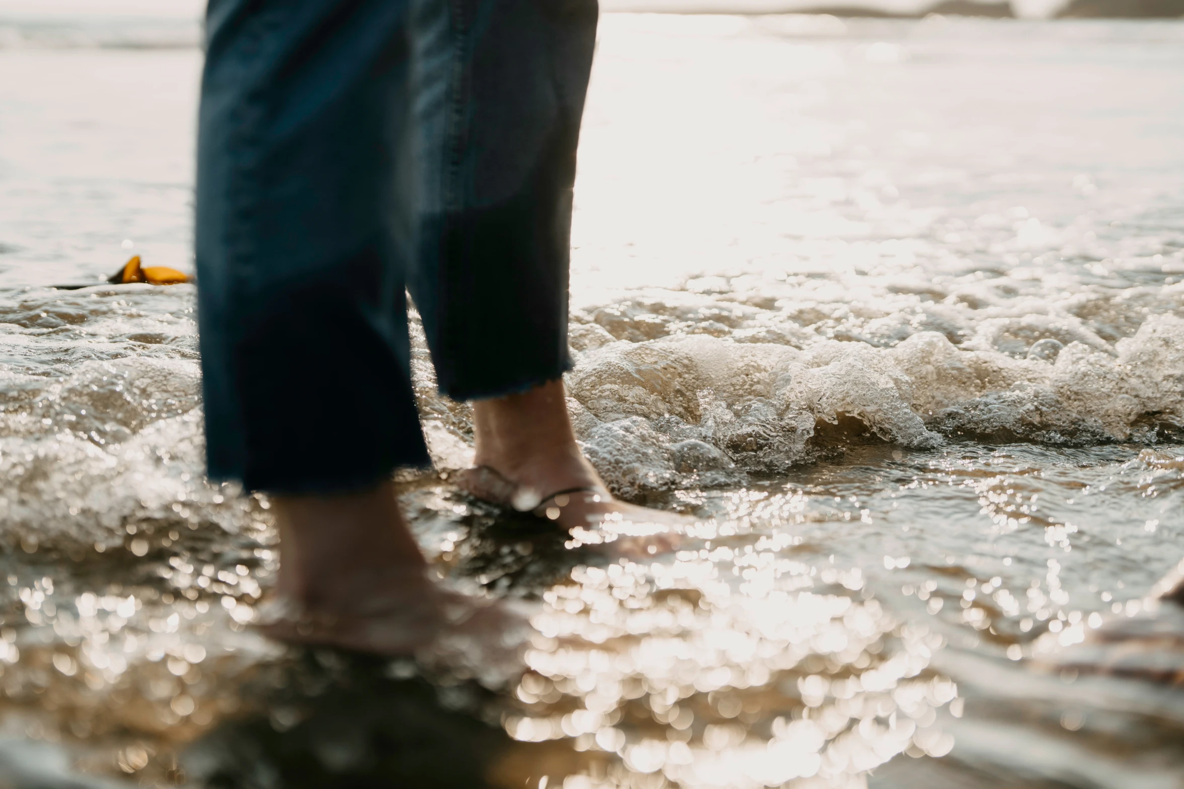 person standing on a beach in water with wave coming ashore