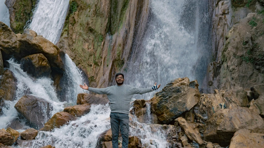 man standing on rocky rock next to a waterfall