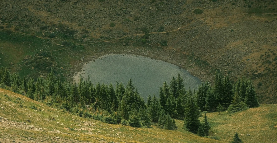a small round lake with trees and hills in the background