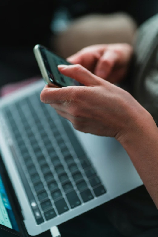 the hands on a laptop are touching a phone