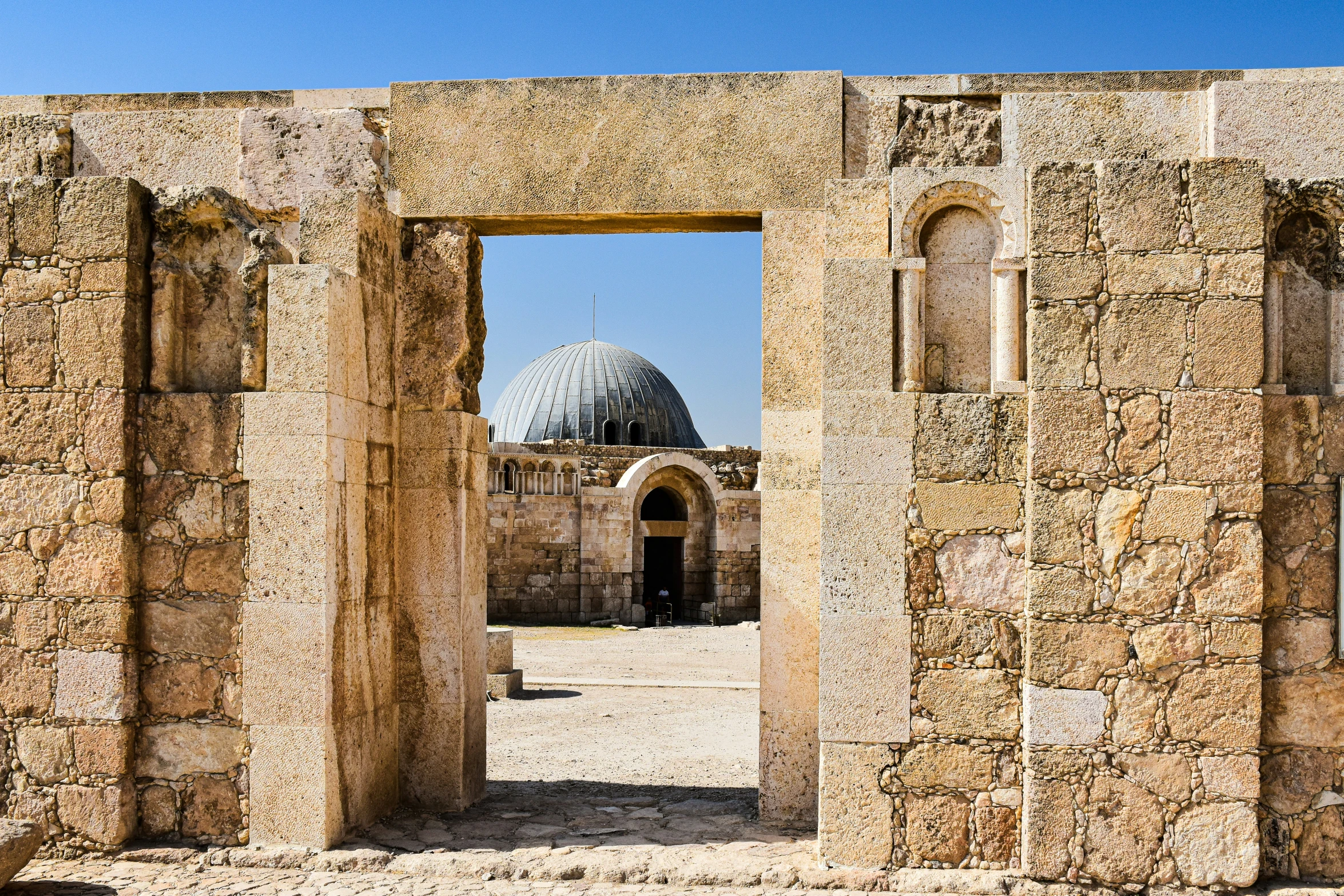 a large archway in a brick wall with a dome behind it