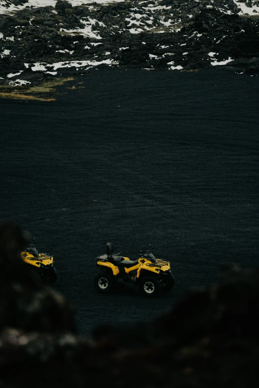 a pair of two small quad bikes parked on black sand