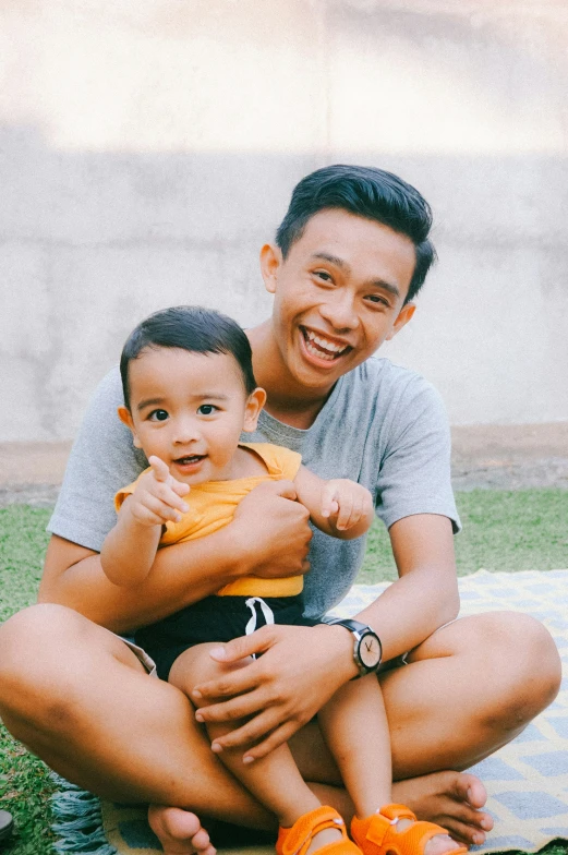 a man holding a baby in front of a child sitting on a blanket