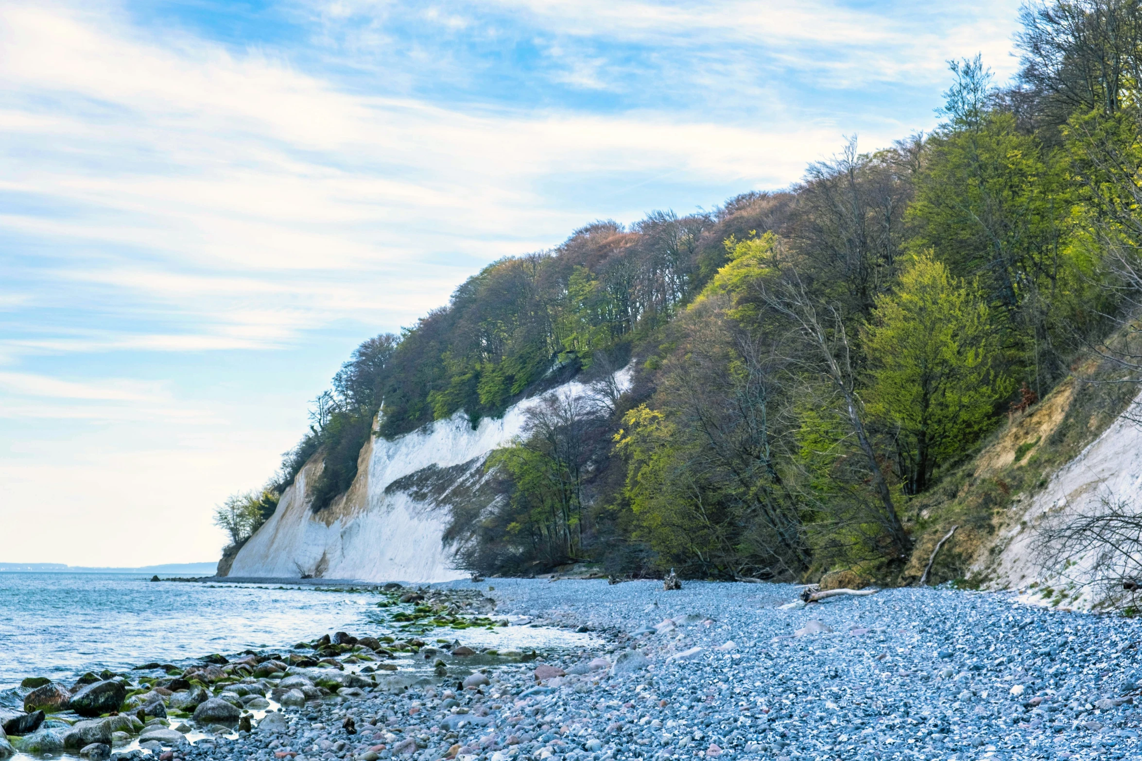 a rocky beach with two people walking on it near the water