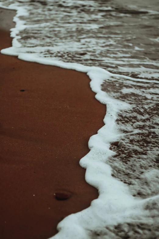 a wave rolls in towards a red sandy beach