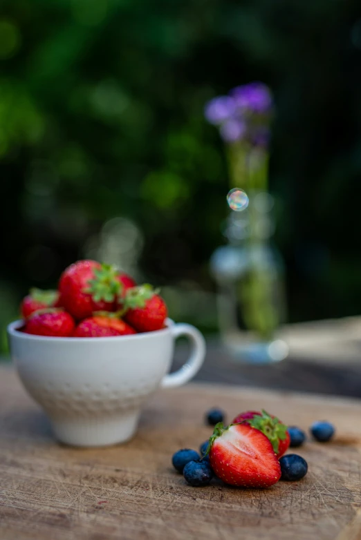 the bowl of strawberries is next to a cup of blueberries