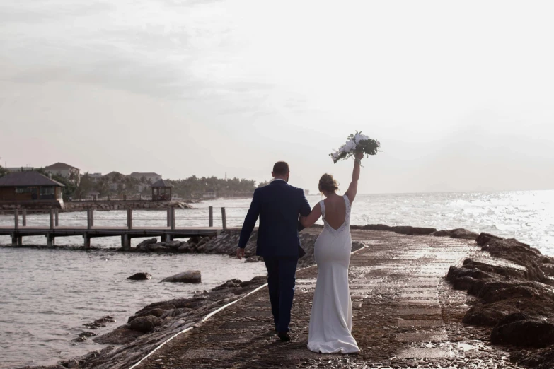 a bride and groom holding a bouquet on the beach