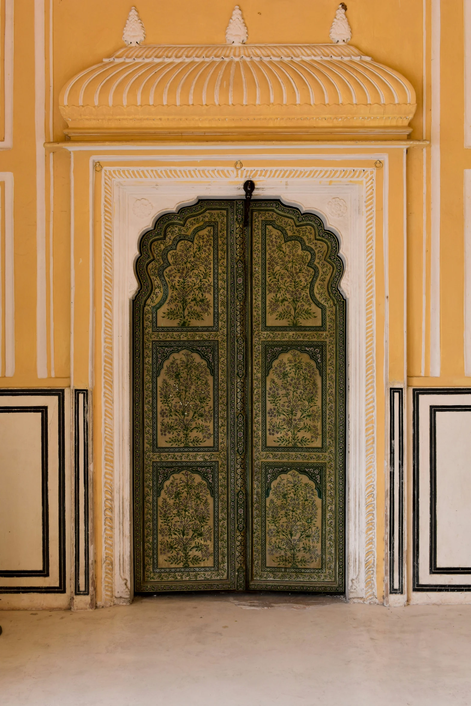 an ornate green door sits in the middle of an intricate yellow and white wall