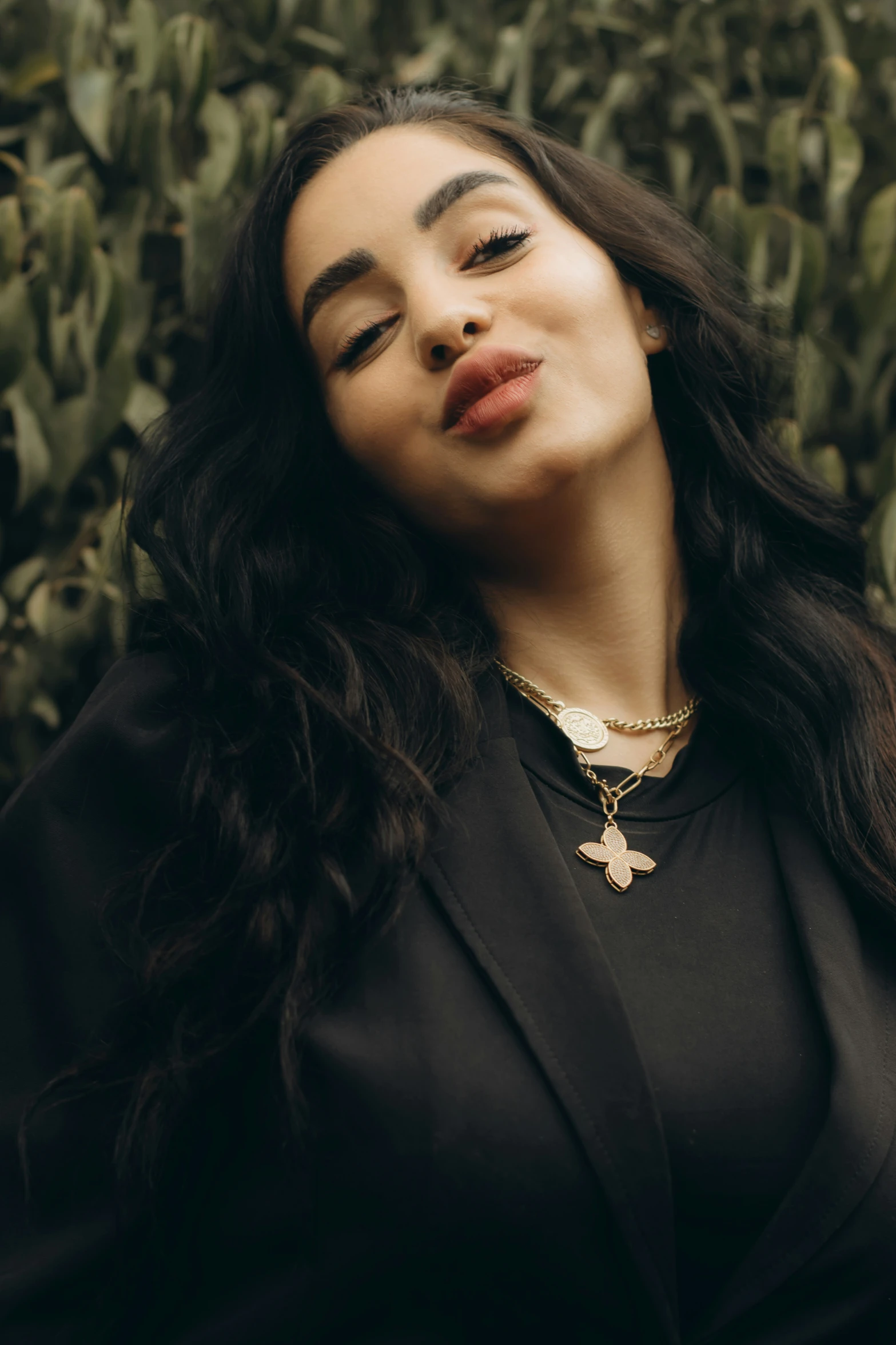 a woman sitting in front of a bush wearing a black jacket