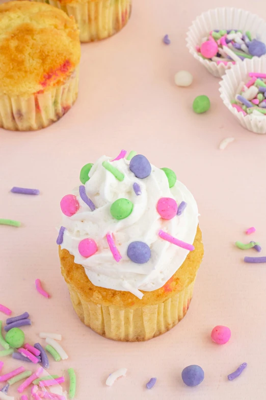 a cupcake with white frosting surrounded by confetti