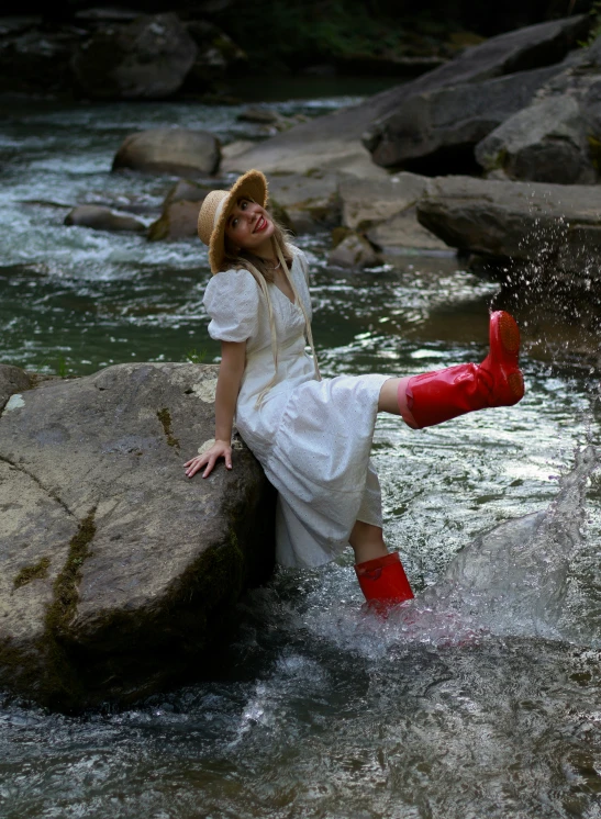 a young woman in red boots is posing on rocks in water