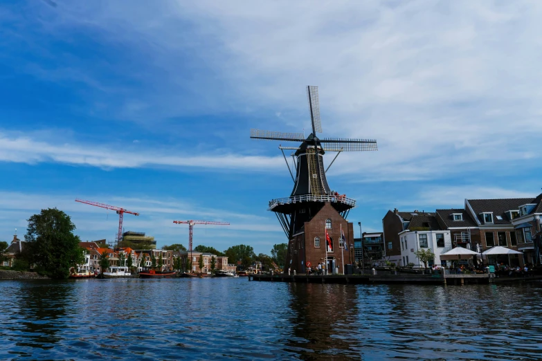 a windmill stands next to several buildings on a water way