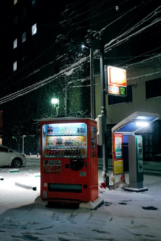 a snowy night at a city street with parking meters, phone booth, and fire hydrant