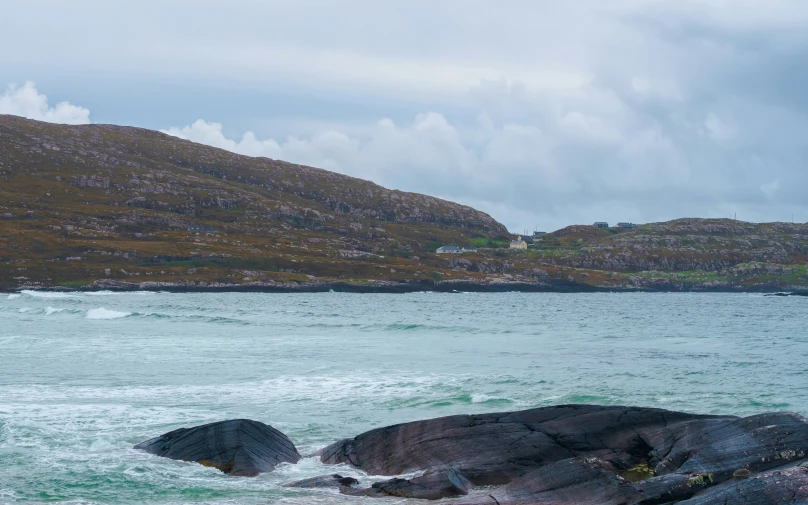 there is a rocky shoreline with water and hills in the background