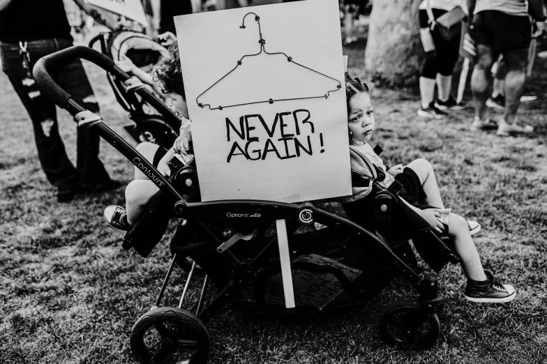 small child with a sign over him sitting in a stroller