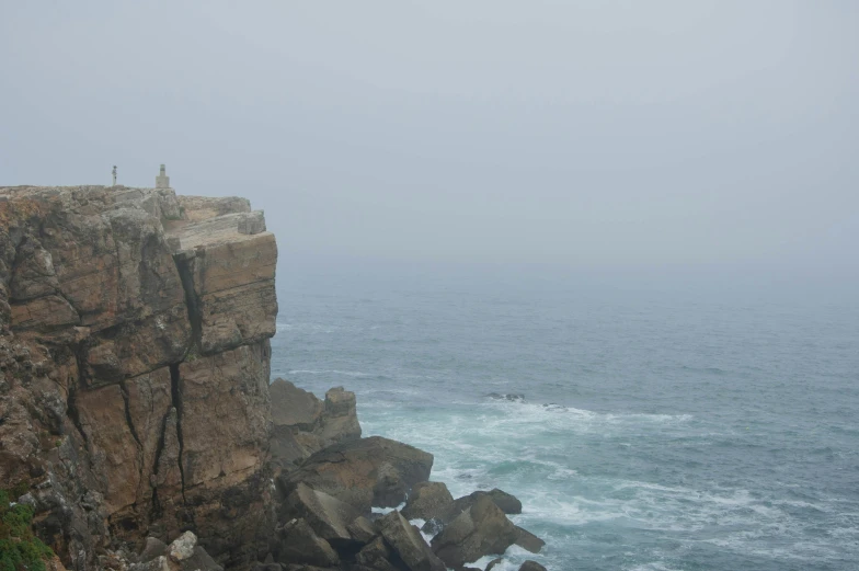 a person sitting on top of a cliff over looking the ocean