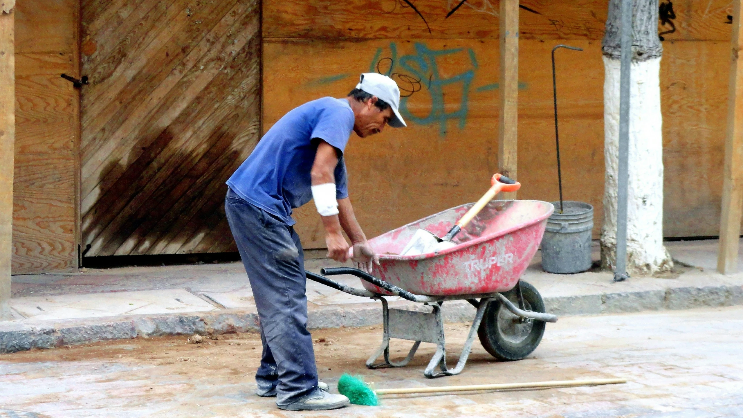 man in blue shirt hing a wheelbarrow with tools