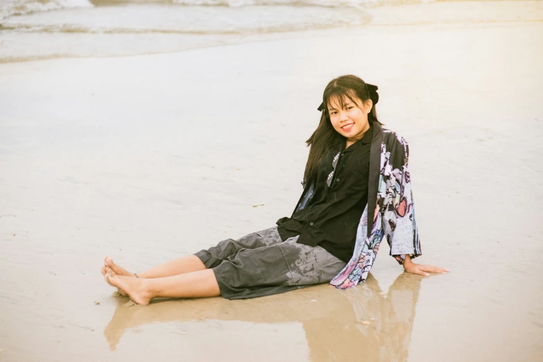 a young woman sitting on the beach, smiling at the camera