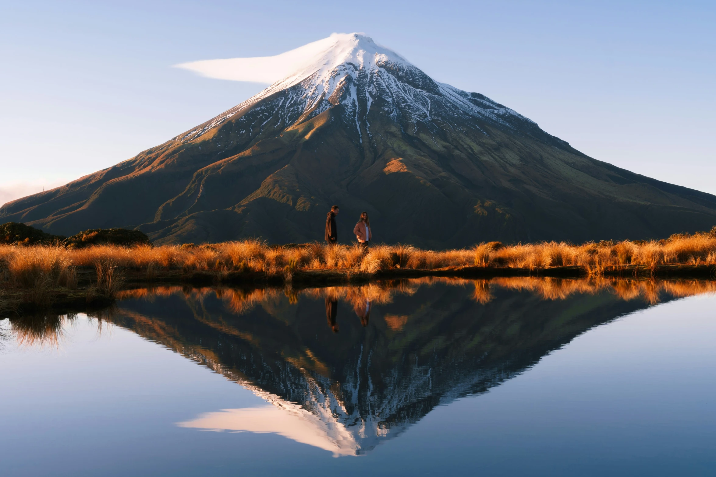 two people standing near a lake watching the mountain