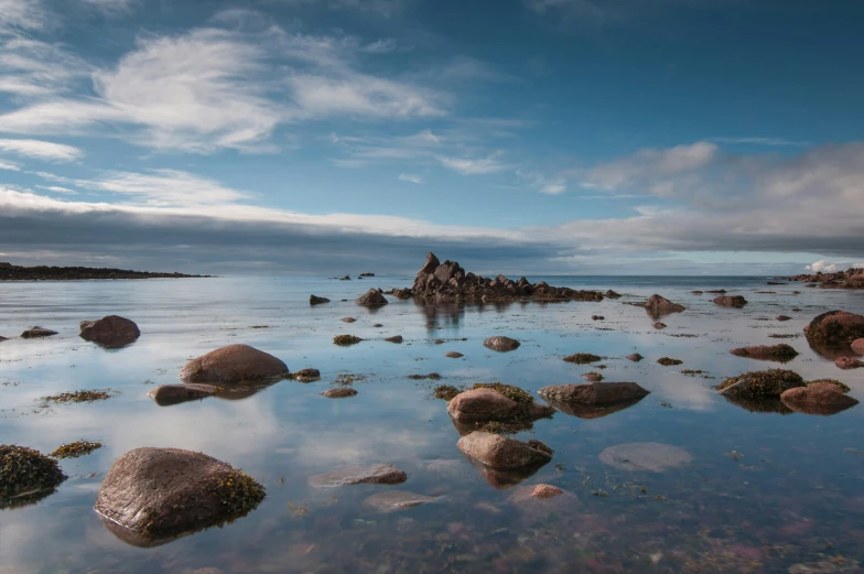 a beach covered with lots of large rocks and shallow water