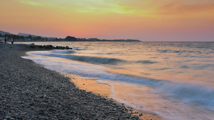 a sunset over a beach as a large body of water crashes into land