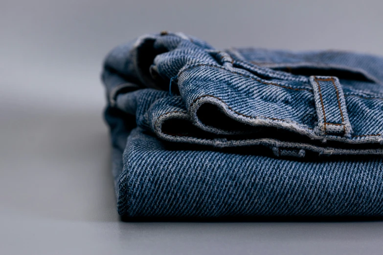 several folded denim jeans, one folded on a white surface