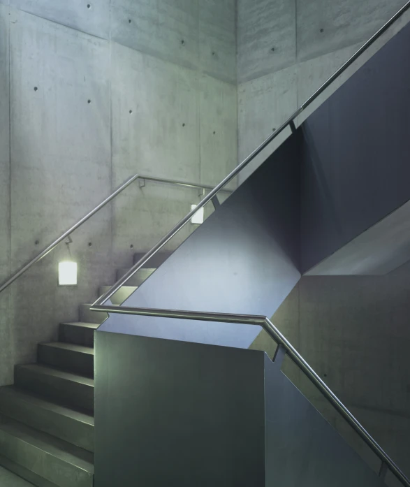 metal steps and railing are positioned beside the concrete walls of an unfinished stairwell