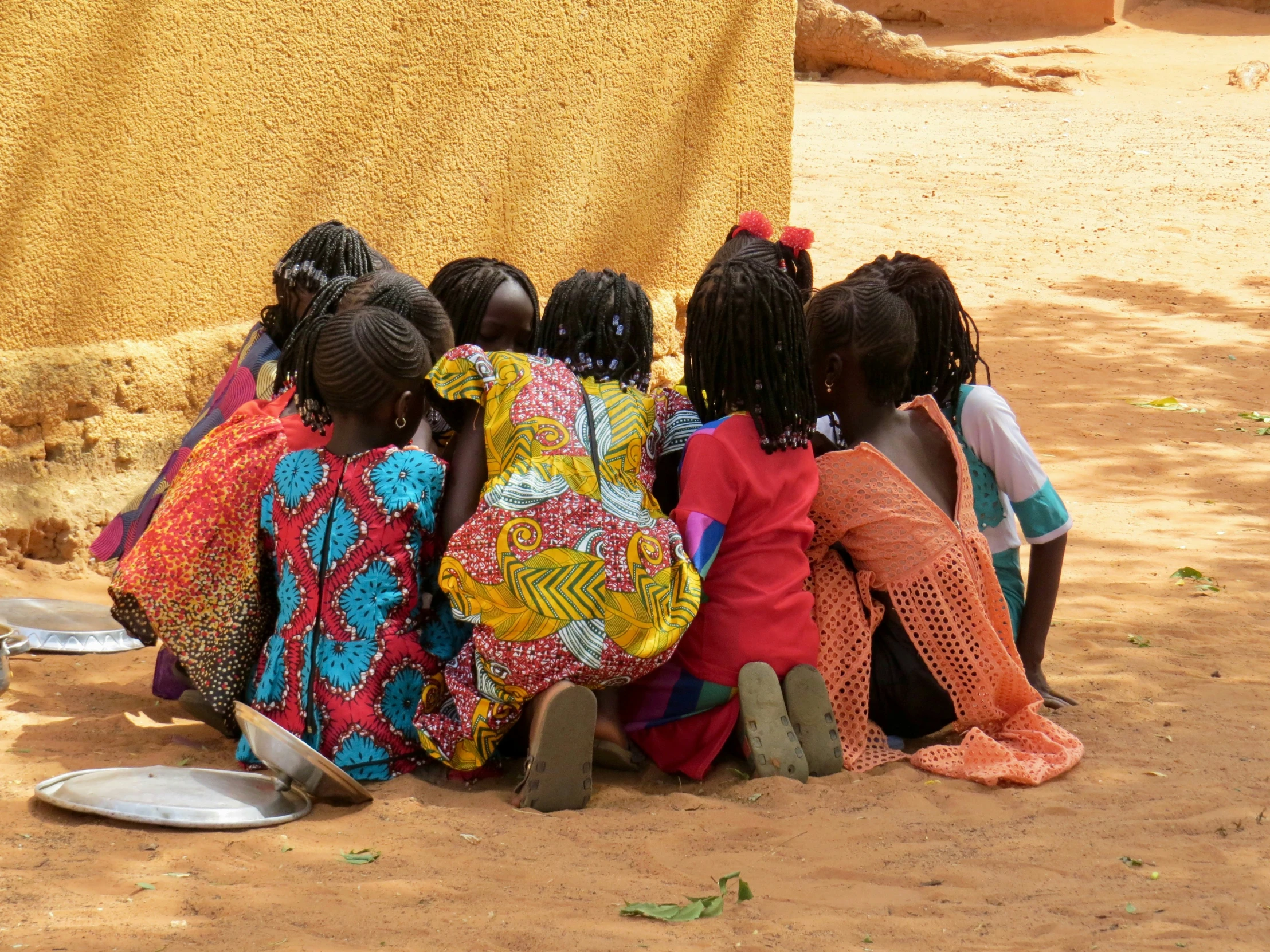 several girls sit in the middle of a village near their kitchen