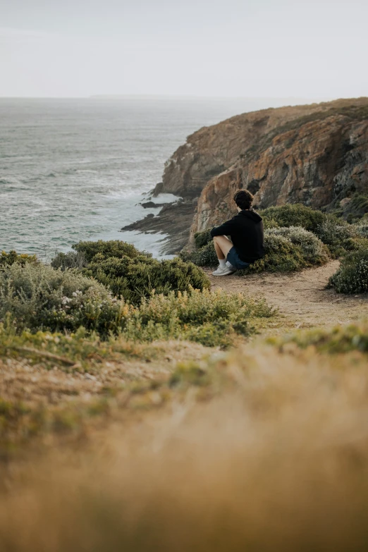 a man is sitting by the ocean looking out at soing